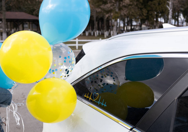 gele en blauwe ballonnen in de kleuren van de Oekraïense vlag bij een witte auto. Ter ondersteuning van Oekraïne. Stop de oorlog in Oekraïne. Onafhankelijkheidsdag, Eenheidsdag - Foto, afbeelding
