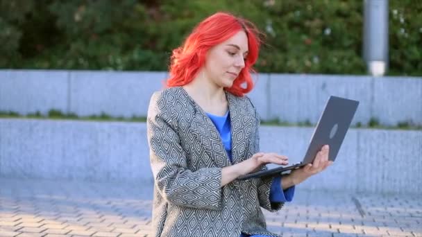 Jeune femme confiante aux cheveux rouges affaires travaillant par ordinateur portable en plein air de la ville coucher de soleil arrière-plan.  - Séquence, vidéo