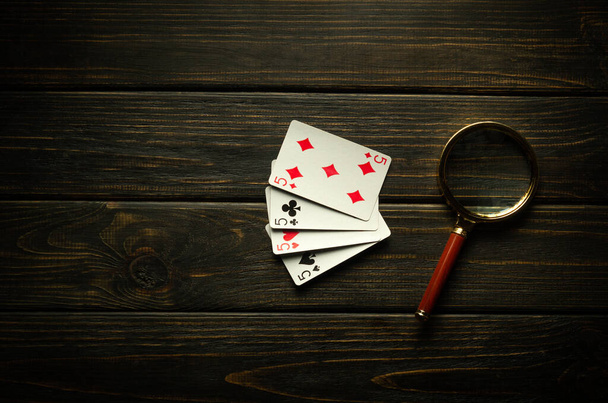 Gra w pokera z czterech w rodzaju lub quadów. Karty do gry i szkło powiększające na czarnym stole vintage w klubie pokerowym. - Zdjęcie, obraz