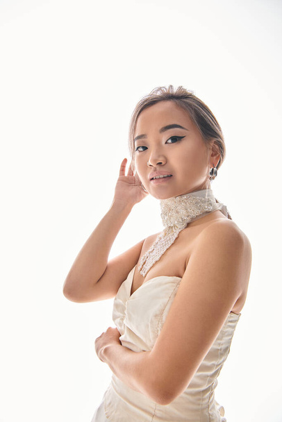 alluring asian bride fixing hairstyle and look to camera against white background - Φωτογραφία, εικόνα