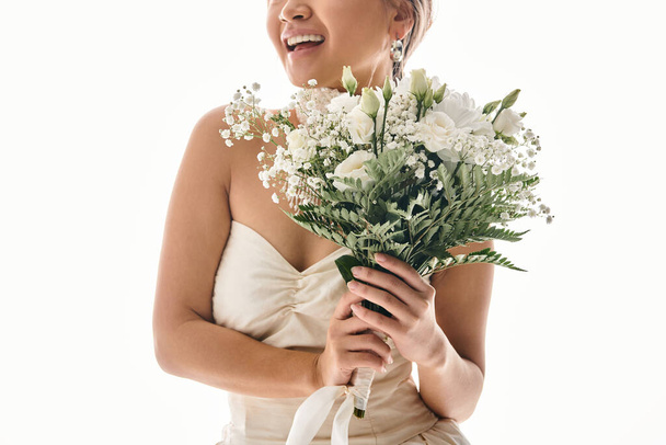 abgeschnittene Aufnahme einer lächelnden jungen Frau mit weißem Blumenstrauß vor hellem Hintergrund - Foto, Bild