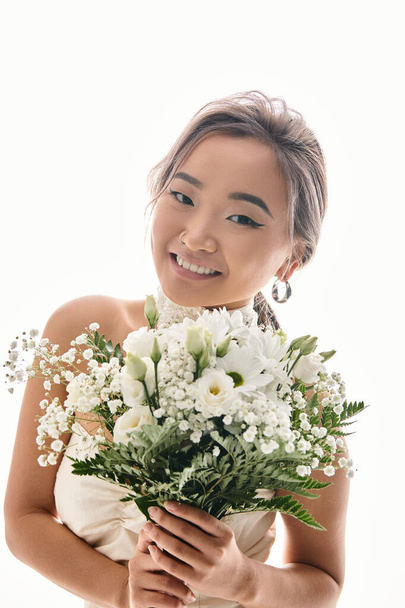 felice seducente asiatica giovane donna sorridente alla macchina fotografica con fiori bianchi bouquet in sfondo chiaro - Foto, immagini