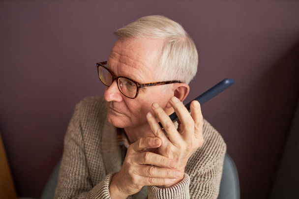 Blind man with gray hair in eyeglasses listening to audio on his mobile phone - Photo, Image