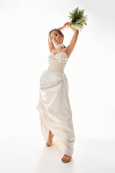 encantador asiático jovem mulher em vestido branco sobre para jogar buquê de flores em fundo leve - Foto, Imagem