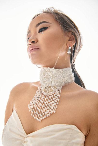 verführerische asiatische junge Frau in weißen Anmut Halskette mit elegantem Make-up auf hellem Hintergrund - Foto, Bild