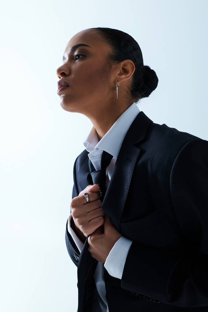 Una joven afroamericana vestida de traje, mira a la distancia con expresión contemplativa. - Foto, imagen