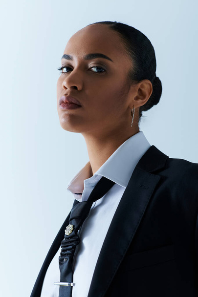 Fiatal afro-amerikai nő öltönyben és nyakkendőben, a stúdió szélén bámul. - Fotó, kép