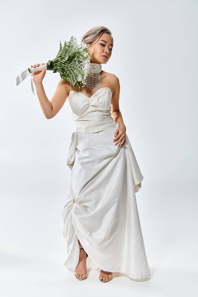 mooie jonge bruid in witte elegante outfit poseren met bloemen boeket en op zoek naar beneden - Foto, afbeelding