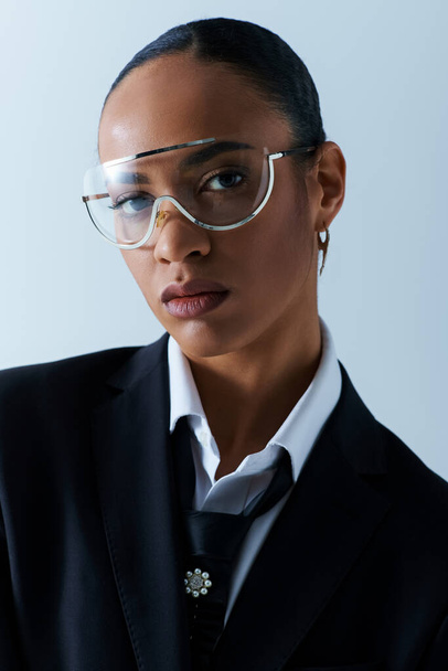 Νεαρή Αφρο-Αμερικανίδα γυναίκα με γυαλιά και κοστούμι σε σκηνικό στούντιο. - Φωτογραφία, εικόνα