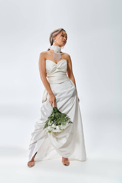 ホワイトエレガントな衣装の魅力的な若い花嫁は,頭を回し,花束でポーズ - 写真・画像