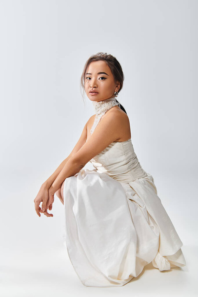 atractivo asiático novia en blanco elegante vestido agachado abajo contra luz fondo - Foto, Imagen