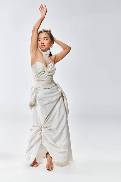 seducente asiatico sposa in bianco grazia abito posa con le mani e cercando di lato su sfondo chiaro - Foto, immagini