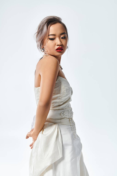 charming asian young woman with red lipstick and pearl necklace looking behind back - 写真・画像