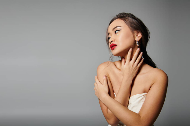 alluring asian woman in white dress with pearl necklace and red lipstick hug herself - Photo, Image