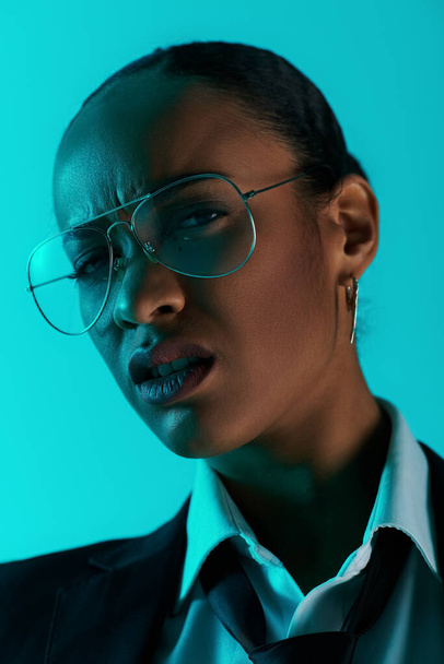Una joven afroamericana en gafas y un traje de pie con confianza en un ambiente de estudio - Foto, imagen