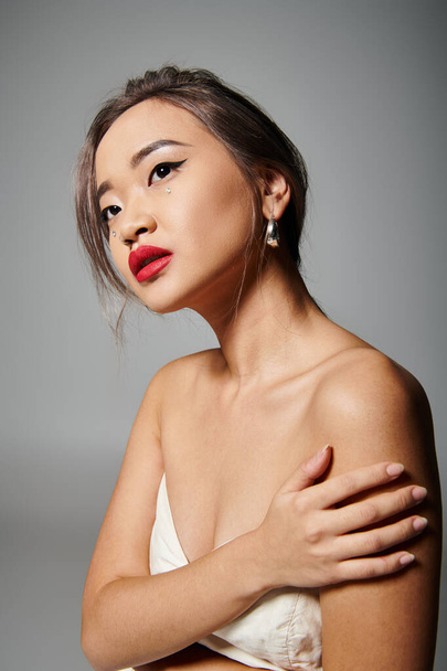 portrait of attractive asian woman holding to shoulder and looking to up on grey background - Foto, Imagem