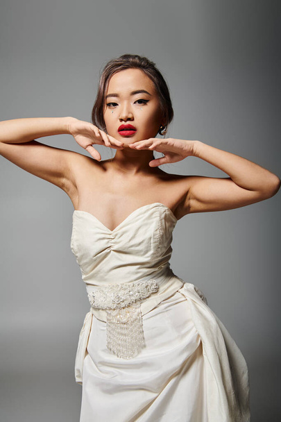 alluring asian bride in her 20s posing with hands in face against grey background - Valokuva, kuva