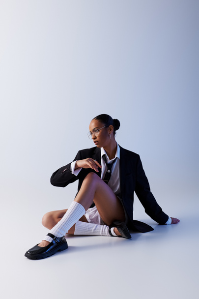 Young African American woman sitting on ground in suit and tie, white studio - Photo, Image