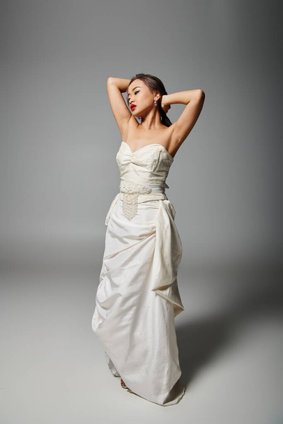 pretty asian woman in white dress with red lips putting hand behind head and looking to down - Photo, Image
