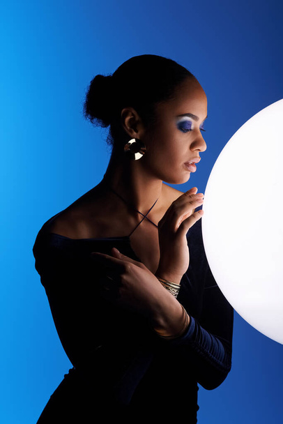 A young African American woman gracefully holds a large white ball in her hands in a studio setting. - Photo, Image