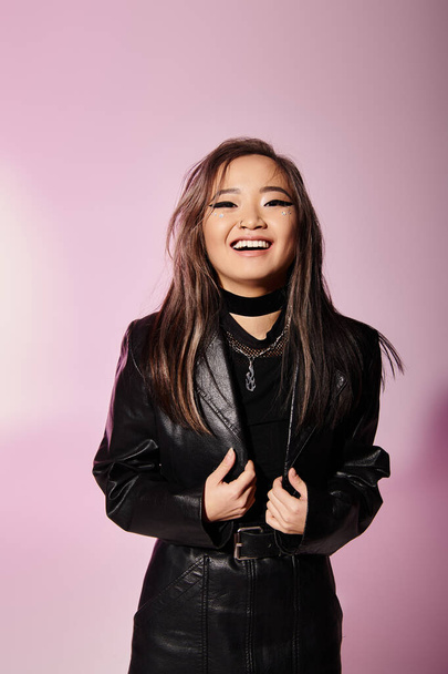 sorrindo asiático mulher no preto couro roupa com pesado maquiagem contra lilás fundo - Foto, Imagem