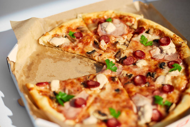 スライスされたトマト,チーズ,キノコ,ハーブが2つのスライスが欠けている新鮮な焼きピザは,屋外のピクニックで共有された食事を示唆しています. - 写真・画像
