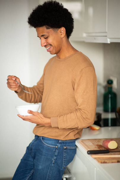 Portrait latéral de jeune homme mangeant dans un bol dans la cuisine - Photo, image