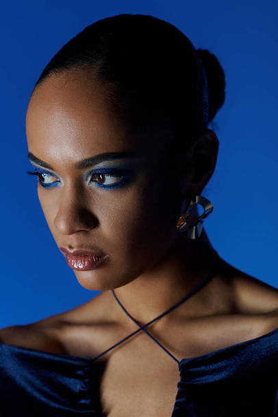Una giovane donna afroamericana in piedi in un abito nero, i suoi occhi blu penetranti accattivante lo spettatore. - Foto, immagini