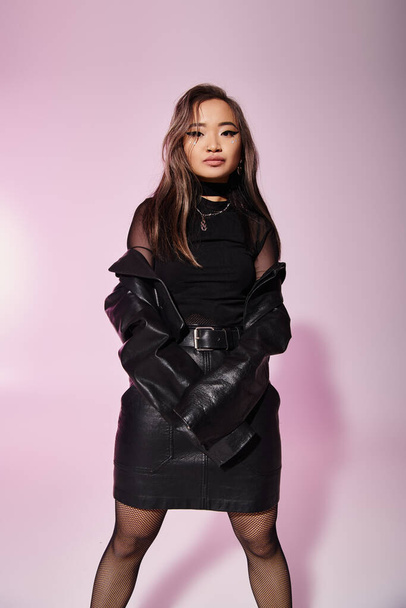 hübsche asiatische junge Frau im schwarzen Lederoutfit posiert vor fliederfarbenem Hintergrund - Foto, Bild