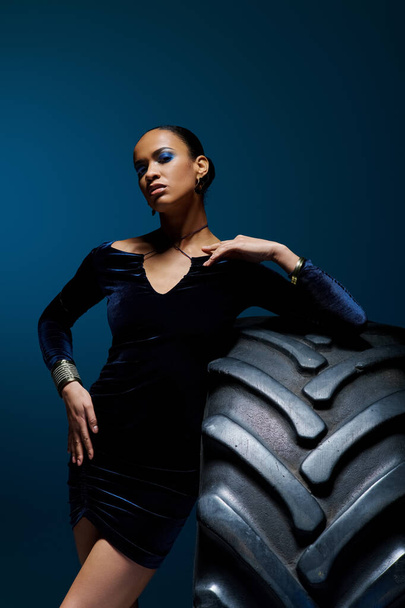 Молодая афроамериканка с решительным выражением лица, уверенно стоящая рядом с гигантской шиной. - Фото, изображение