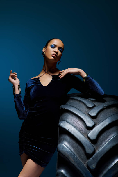 Молодая афроамериканка уверенно стоит рядом с огромной шиной в студии. - Фото, изображение