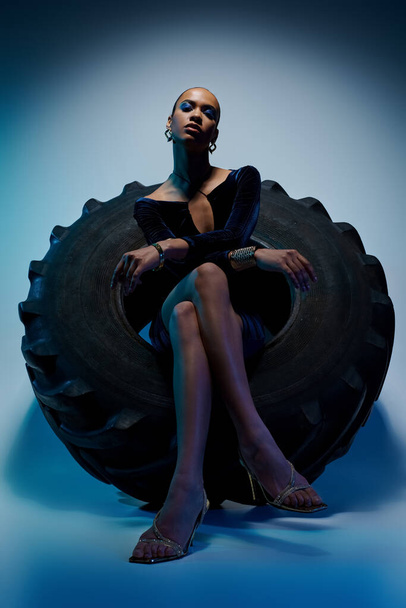 アフリカ系アメリカ人の若い女性は,クリエイティブスタジオの設定で巨大なタイヤの上に自信を持って座ります. - 写真・画像