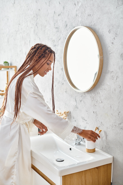 Μια Αφρο-Αμερικανίδα με αφρο-πλεξούδες πλένει τα χέρια της σε ένα μοντέρνο μπάνιο, ασκώντας προσωπική υγιεινή και αυτοφροντίδα.. - Φωτογραφία, εικόνα