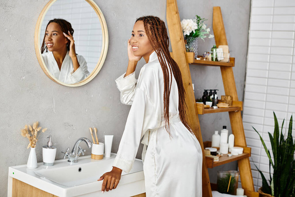 Eine afroamerikanische Frau mit Afro-Zöpfen steht in einem modernen Badezimmer vor einem Spiegel - Foto, Bild