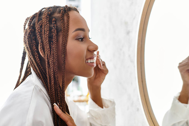 Uma mulher afro-americana com tranças afro usando almofada de algodão em um banheiro moderno, focada em sua rotina diária de beleza. - Foto, Imagem