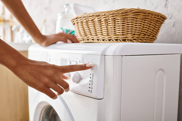 Африканська американка з афро косами натискає кнопку на пральну машинку роблячи прання у ванній. - Фото, зображення