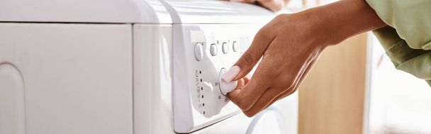 Afro-Amerikalı bir kadın banyodaki çamaşır makinesine kurutma makinesi yüklüyor. - Fotoğraf, Görsel