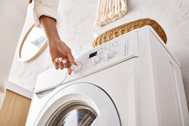 Eine Afroamerikanerin drückt einen Knopf an einer Waschmaschine im Badezimmer und wäscht. - Foto, Bild