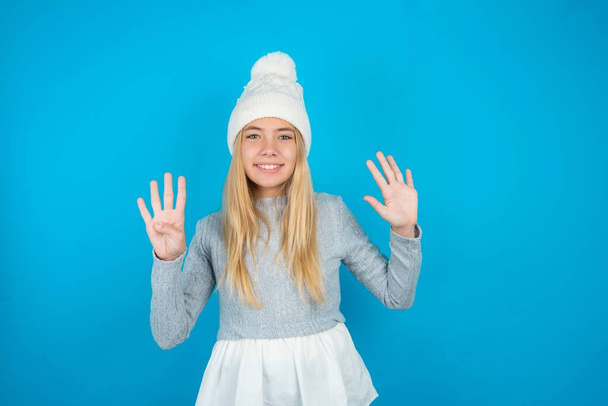 Krásné dítě dívka na sobě bílý pletený klobouk a modrý svetr ukazující a ukazující nahoru s prsty číslo devět při úsměvu sebevědomě a šťastně. - Fotografie, Obrázek