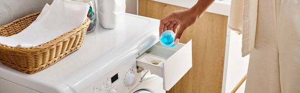 Afrikalı Amerikalı bir kadın banyoda mavi jel kapsül kullanarak çamaşır makinesini temizliyor.. - Fotoğraf, Görsel