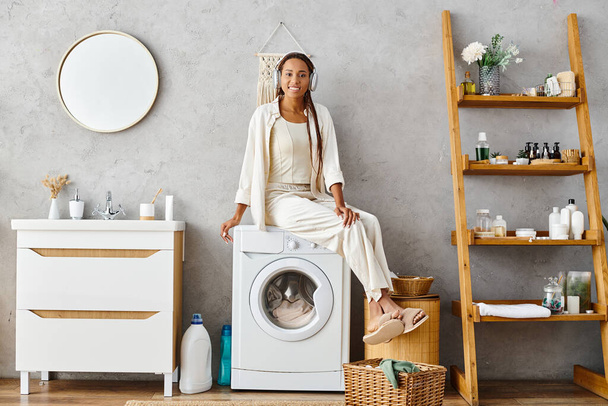 Eine afroamerikanische Frau mit Afro-Zöpfen sitzt selbstbewusst auf einer Waschmaschine und wäscht im Badezimmer. - Foto, Bild