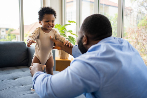 Portrét šťastného afrického amerického otce s roztomilou holčičkou na gauči doma v obývacím pokoji, starostlivý otec se usmívá a baví svou dívku, zatímco sedí na gauči, šťastná rodina - Fotografie, Obrázek