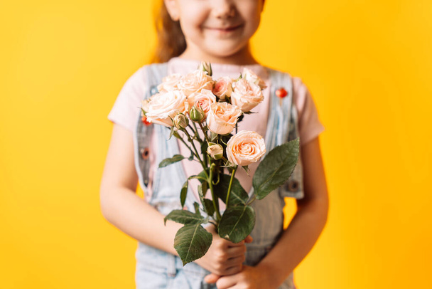 Little girl holding spray roses in her hands against yellow background. - Photo, Image