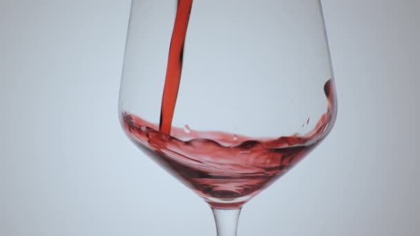 Червоне вино утворює красиву хвилю. Вино наливається в келих для вина на білому тлі. Крупним планом постріл. - Кадри, відео