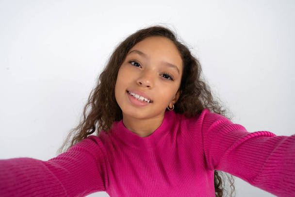 Foto di Bella bambina che indossa dolcevita rosa su sfondo bianco fare selfie - Foto, immagini
