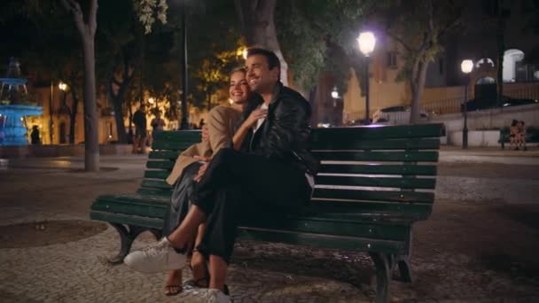 Milý pár sedící na lavičce v parku, mazlící se na večerním rande. Šťastní manželé, co spolu odpočívají v noci. Usmívající se pohledný muž objímající radostnou ženu venku. Urban romance relationship concept. - Záběry, video