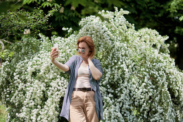 Estilo de vida independiente en plena floración - mujer joven captura su momento entre flores blancas. - Foto, imagen