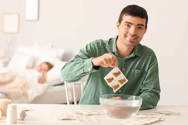 Young man dipping mustard plaster into bowl of water in bedroom - Foto, Imagem