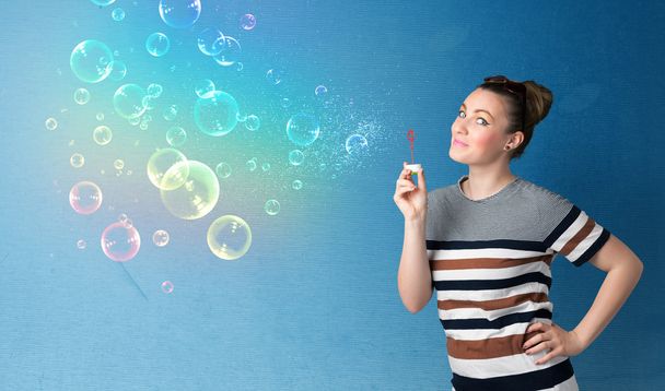 Pretty lady blowing colorful bubbles on blue background - Fotó, kép