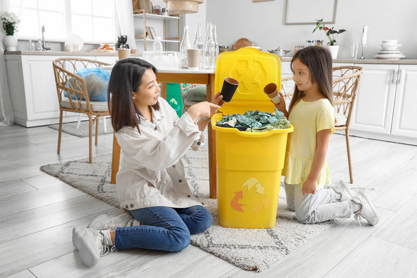 Madre asiática con su hija pequeña tirando vasos de papel en la papelera de reciclaje en casa - Foto, imagen